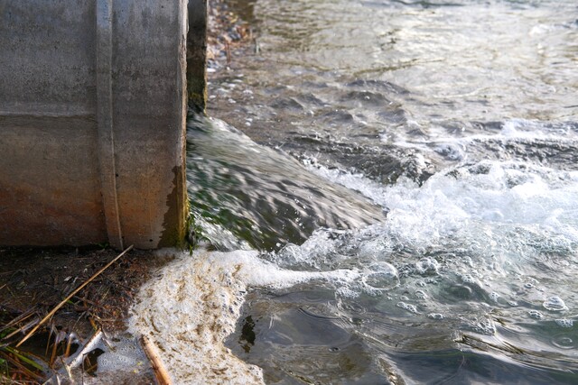Large concrete outfall pipe, discharging water or treated effluent into river or pond with foam and debris. Wastewater from sewage treatment plants, environmental concept